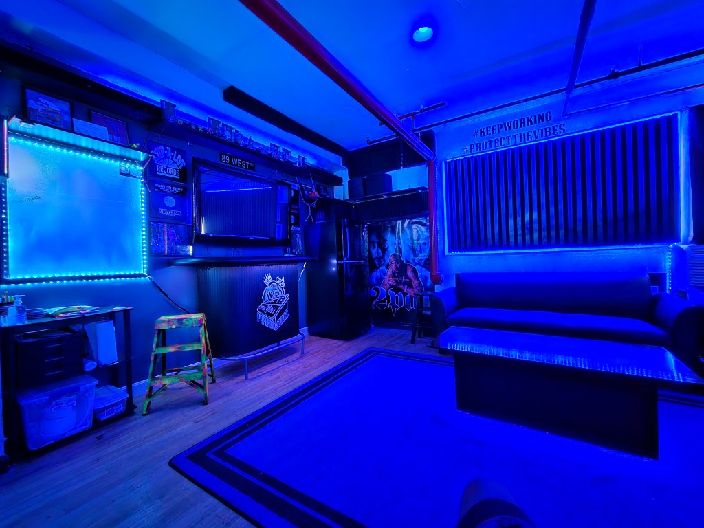 Blue-lit studio lounge with whiteboard, bar area, and #KEEPWORKING wall art