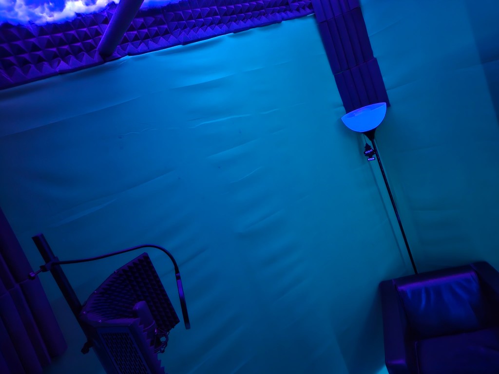 Blue-lit vocal booth with microphone, pop filter, and acoustic treatment